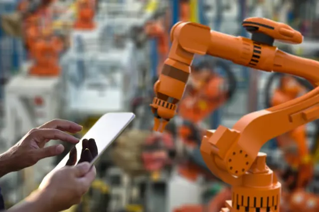 Manufacturing machinery and a person holding a tablet. Manufacturing machinery and a person holding a tablet.