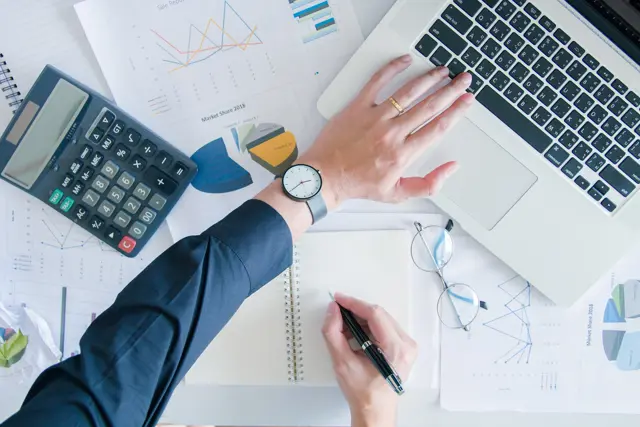 Hand on a desk with a laptop, calculator and documents Hand on a desk with a laptop, calculator and documents