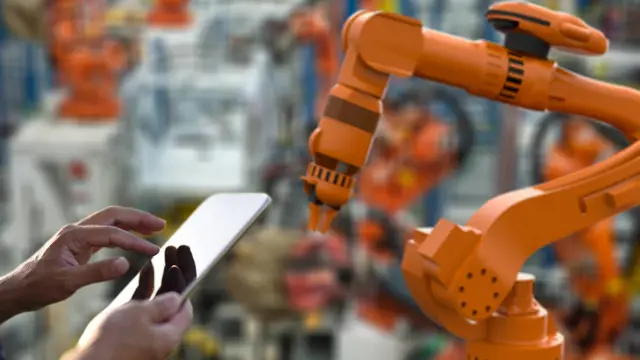 Manufacturing machinery and a person holding a tablet.  Manufacturing machinery and a person holding a tablet.