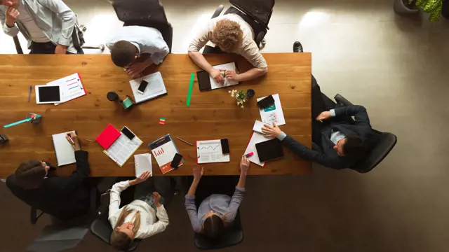 People working around a wooden table together and looking at data People working around a wooden table together and looking at data