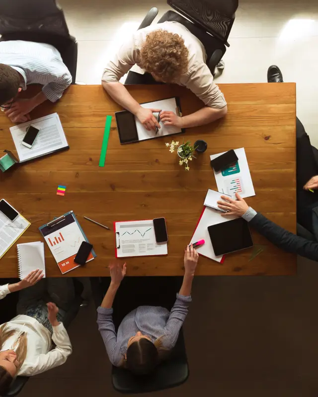 People working around a wooden table together and looking at data People working around a wooden table together and looking at data